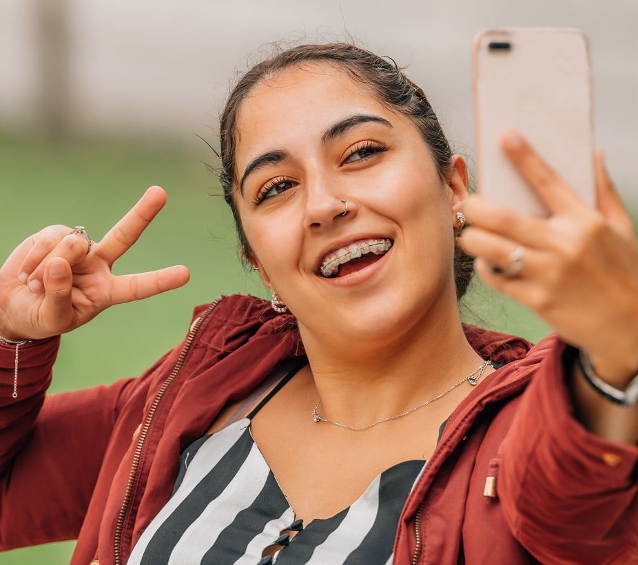 Girl with Braces Taking Selfie A happy young woman with braces taking a selfie and flashing a peace sign outdoors