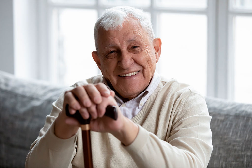 Elderly Man with Bright Smile - Ultra Dental A senior man holding a cane, smiling warmly and showcasing healthy teeth - Ultra Dental.