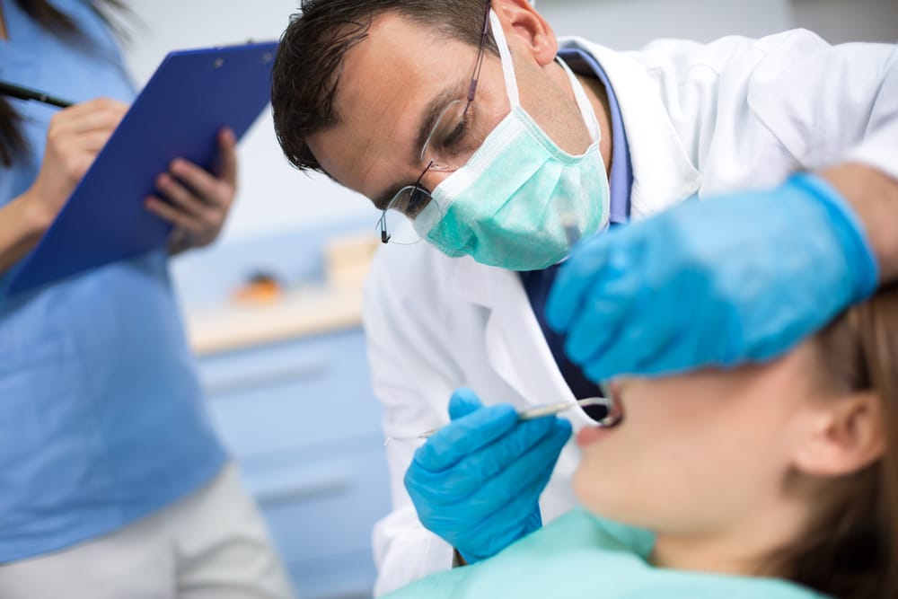 Dentist performing a root canal procedure on a patient while wearing gloves, mask, and protective eyewear in a clinical setting.