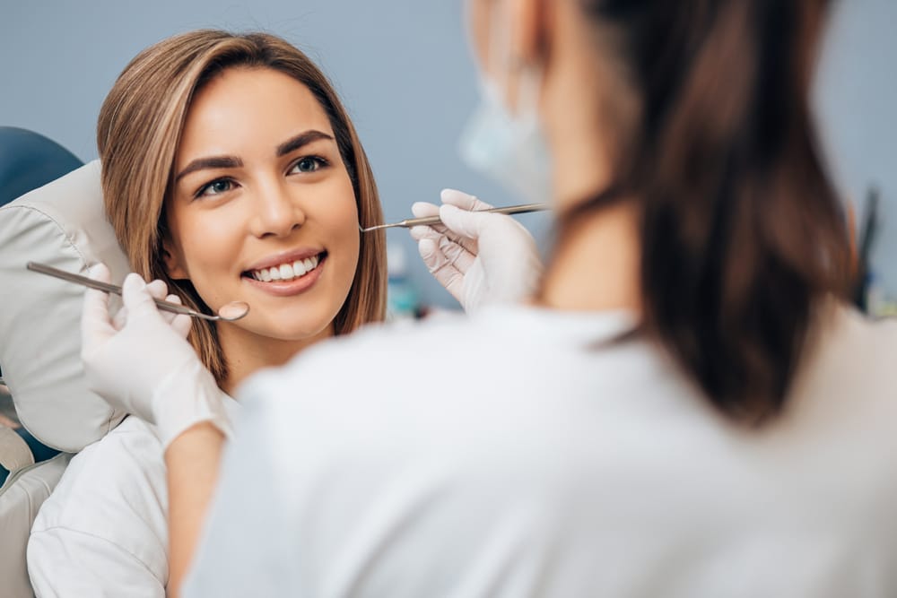 Dentist examining a smiling female patient during a dental checkup, potentially screening for signs of mouth cancer.