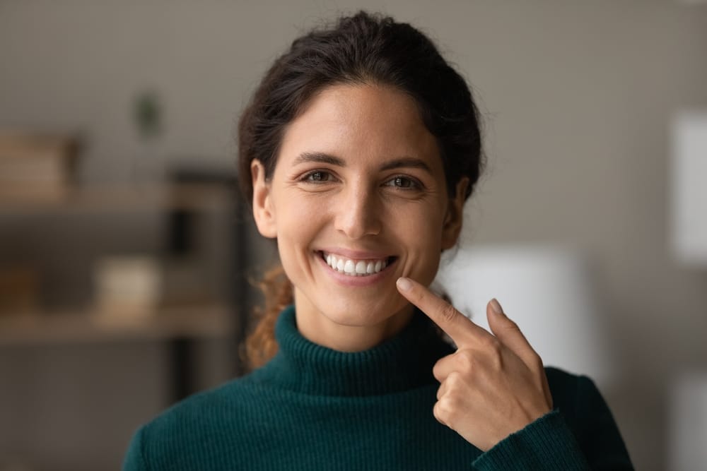 A cheerful woman points to her beautiful smile, highlighting the importance of oral health and confidence. Bright smiles start here. - Dentist in South Gate, CA