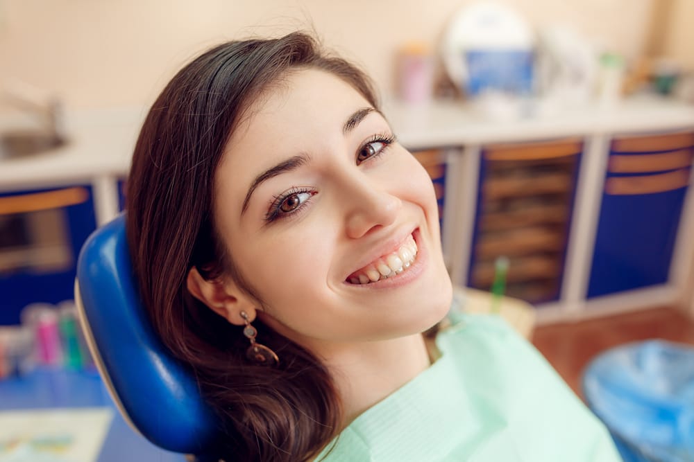Smiling female patient sitting in a dental chair after a checkup, possibly receiving treatment or evaluation for gingivitis.