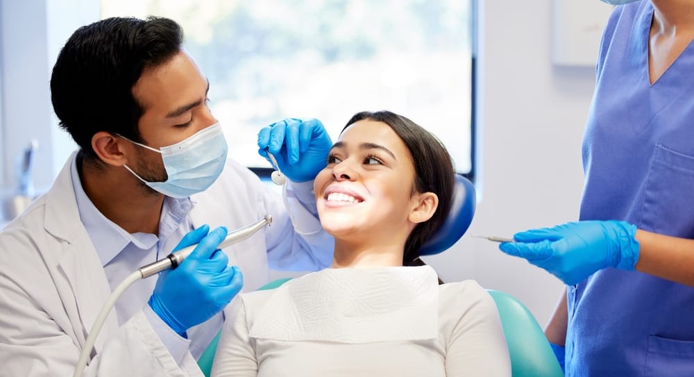 Dentist preparing to apply dental sealants on a smiling female patient during a preventive dental visit in a modern clinic.