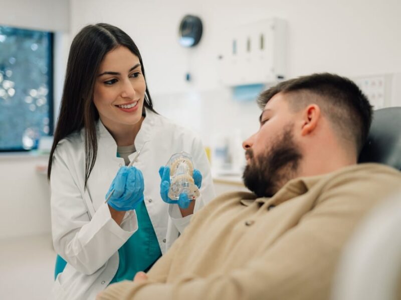 Smiling,Female,Dentist,Holding,Dental,Mold,And,Pointing,At,It