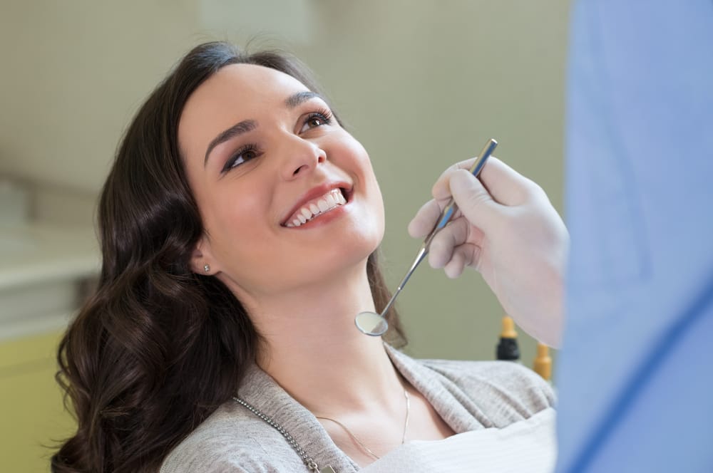 A happy daughter with glasses hugs her smiling mother from behind on the couch, capturing a warm and joyful family moment – Orthodontist Sylmar