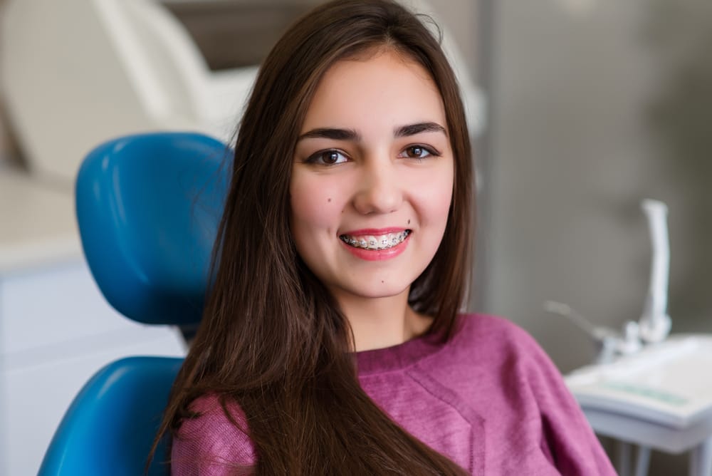 Teen Girl with Braces Smiling in Dental Chair – Emergency Dentist in San Fernando, CA A young girl with braces smiles confidently while seated in a dental chair, showcasing a positive orthodontic visit even during unexpected dental concerns – Emergency Dentist in San Fernando, CA.