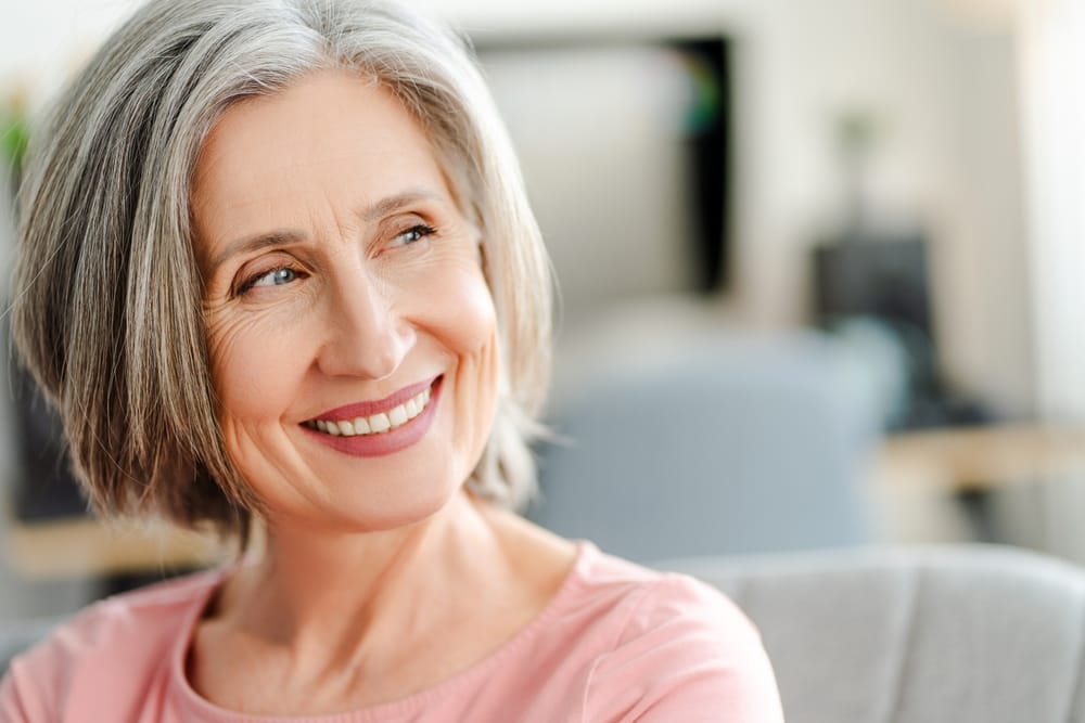 Smiling Senior Woman Looking to the Side – Dentist in Pacoima, CA A joyful older woman with gray hair smiles warmly while looking off to the side, showcasing confidence and comfort in her healthy smile – Dentist in Pacoima, CA.