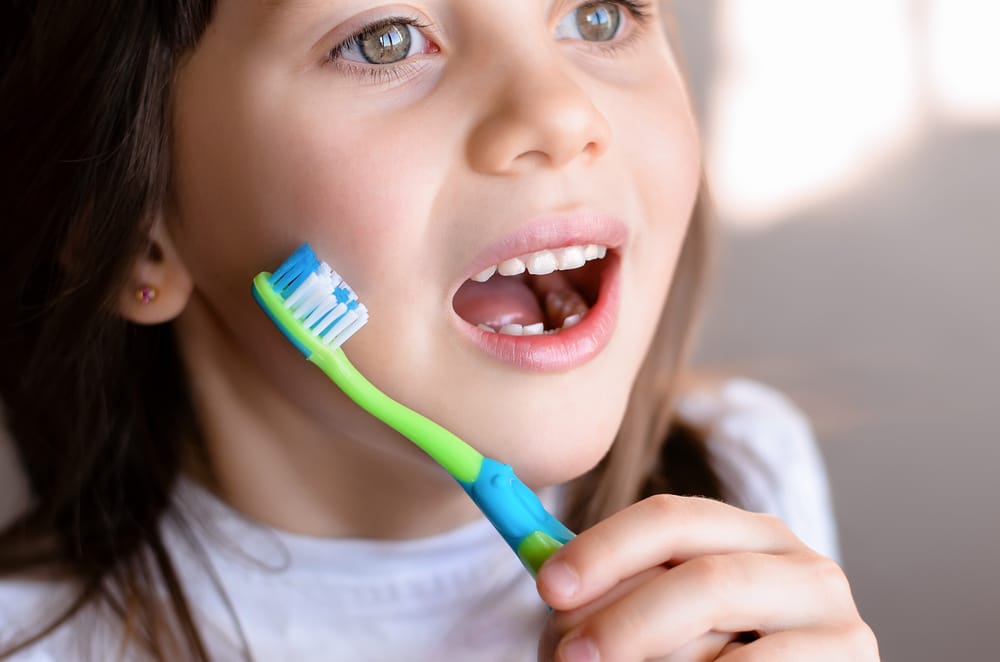 A close-up of a young girl brushing her teeth with a colorful toothbrush, practicing healthy dental habits at home – Pediatric Dentist in San Fernando.
